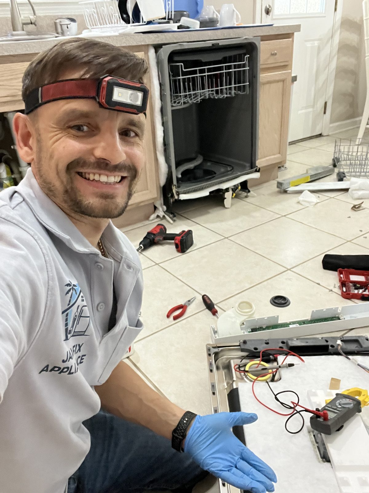 Konstantin kneeling by a pulled-out dishwasher with tools and parts laid out