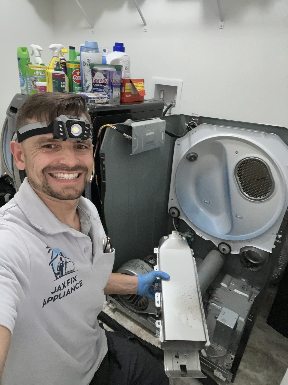 Konstantin holding the heater housing beside an opened dryer in a laundry room