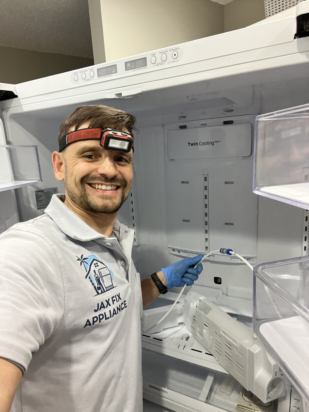 Konstantin in branded Jax Fix Appliance polo servicing the water line inside a Samsung Twin Cooling refrigerator